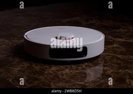 A white robot vacuum cleaner on a brown tile Stock Photo