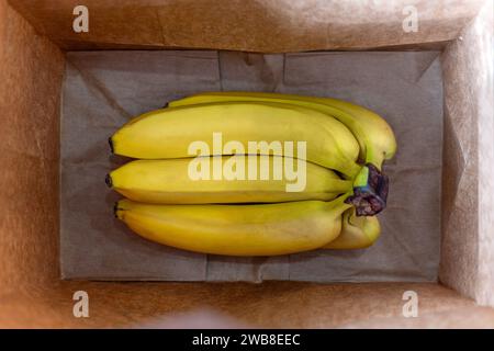 a bunch of bananas in a brown paper bag top view. Buying bananas at the store or harvesting. Stock Photo