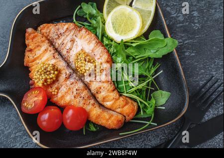 Grilled Butterfly salmon steak with cherry tomatoes and arugula salad on a black square plate. Black plate for serving the dish. Close-up Stock Photo