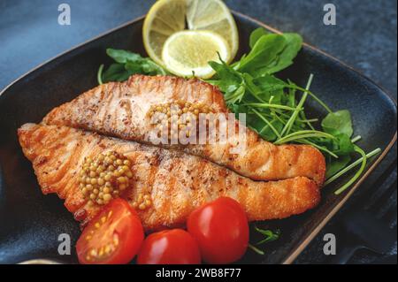 Grilled Butterfly salmon steak with cherry tomatoes and arugula salad on a black square plate. Black plate for serving the dish. Close-up. Stock Photo