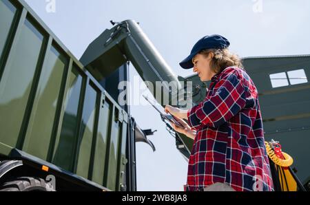 Woman farmer with tablet watching grain loading. Stock Photo