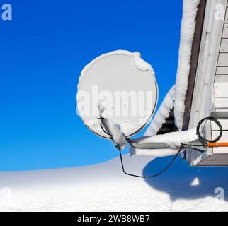 Satellite dish aerial antenna covered with snow, against of the blue sky. Stock Photo