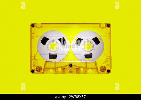 Clear plastic retro audio cassette with spools, isolated on yellow background in close up. The picture is intended for design work on the theme of mus Stock Photo