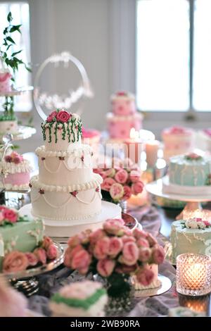 Elegant white wedding cake decorated with pink flowers on a dessert table at a wedding reception. Stock Photo
