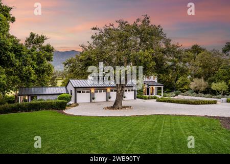 An idyllic modern house in a peaceful rural setting, boasting an expansive front yard with lush green grass and trees Stock Photo