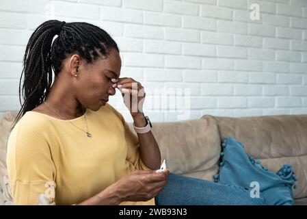 African American woman sitting at home in apartment having issue and headache because of loud noise coming from apartment above. Sick or ill female, n Stock Photo