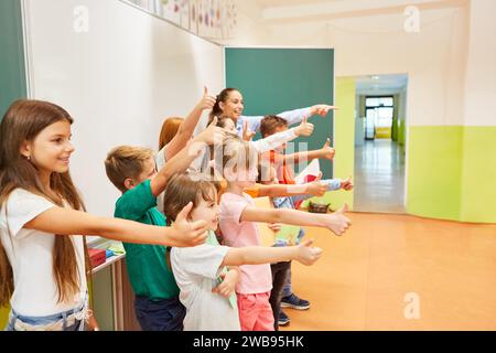 Group of cheerful students making thumbs up gesture while standing with teacher in classroom Stock Photo