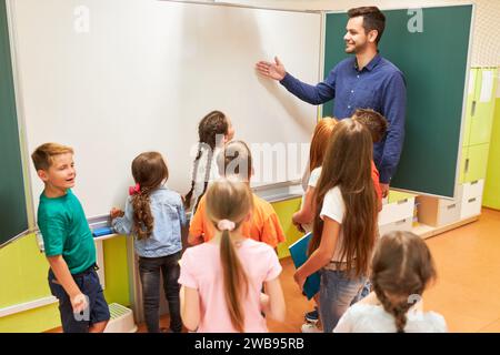 Smiling elementary teacher explaining students over whiteboard in classroom Stock Photo