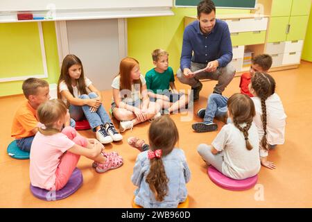 High angle view of male teacher crouching by students sitting on classroom floor Stock Photo