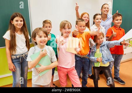 Portrait of happy male and female students showing thumbs up gesture while standing with teacher in classroom Stock Photo