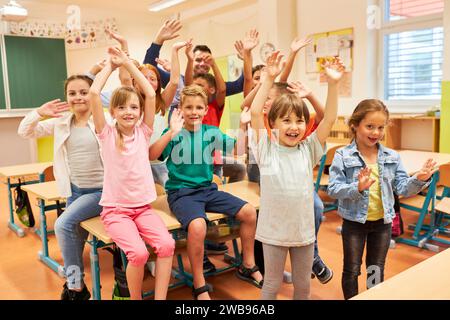 Group of male and female elementary students waving in classroom at school Stock Photo