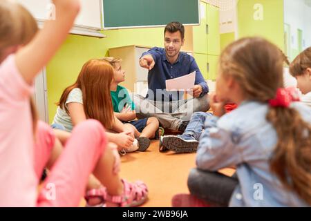 Elementary school teacher sitting in circle with group of students in classroom Stock Photo