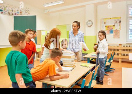 Female teacher stacking books on bench with group of students in classroom Stock Photo