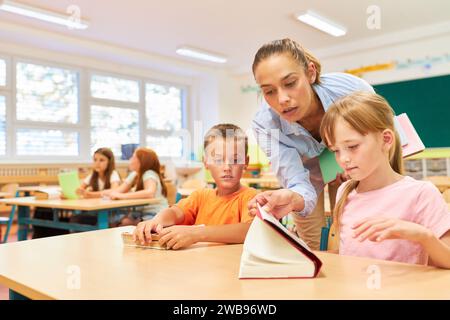 Female teacher reading book to students sitting on bench in classroom at school Stock Photo