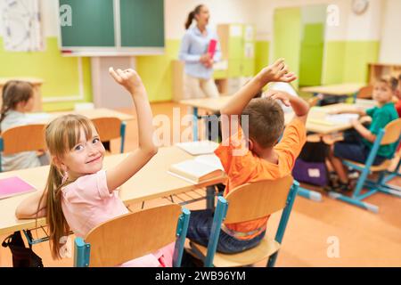 Smiling schoolgirl looking away with hand raised during lecture in classroom Stock Photo