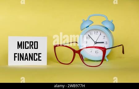 The text MICRO FINANCE is written in a notepad. View of glasses and watches on a yellow background. Business concept Stock Photo