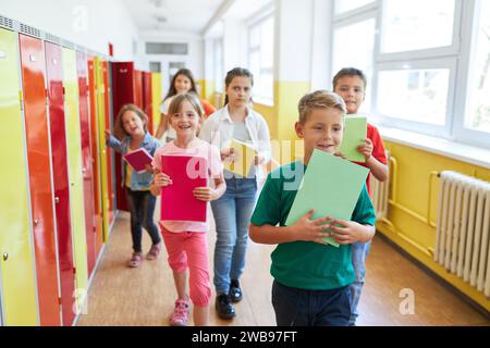 Male and female schoolkids walking while holding books near lockers in hallway Stock Photo