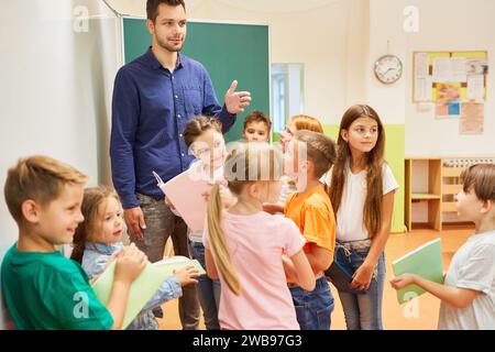 Male and female school students holding books while standing with teacher in classroom Stock Photo