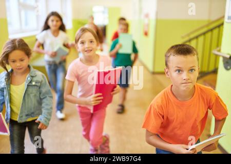 Happy male and female kids running in school hallway during recess Stock Photo