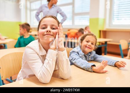 Portrait of smiling schoolgirl leaning on desk while sitting with friend in classroom at school Stock Photo
