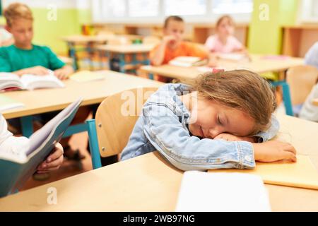 Tired elementary schoolgirl sleeping on bench in classroom Stock Photo