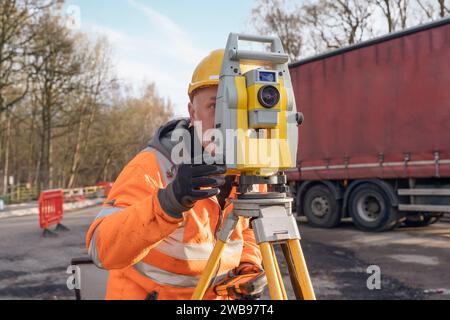 Site engineer operating his instrument during roadworks. Builder using total positioning station tachymeter on construction site for new road setting Stock Photo