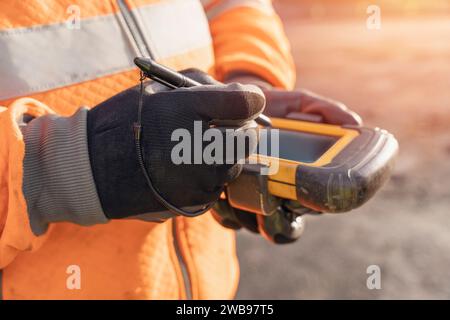 Site engineer operating his touch screen controller instrument during roadworks. Builder using touch screen controller to control total positioning st Stock Photo