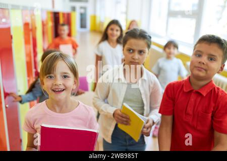 Group of happy elementary kids standing near lockers in hallway at school Stock Photo
