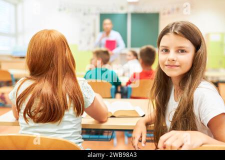 Portrait of smiling elementary schoolgirl sitting with female friend in classroom Stock Photo