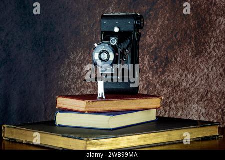 Vintage folding film camera on a pile of old books on a wooden shelf Stock Photo