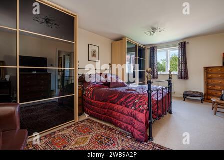 Cambridge, England - Sept 16 2015: Furnished master bedroom with red quilt and mirrored wardrobes Stock Photo