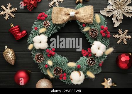 Wreath from fir, pine and spruce twigs, decorated with cotton, flowers ad christmas decoration on black wooden background. Top view Stock Photo