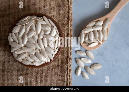 A bowl with spoon full of pumpkin seeds,on light blue background Stock Photo