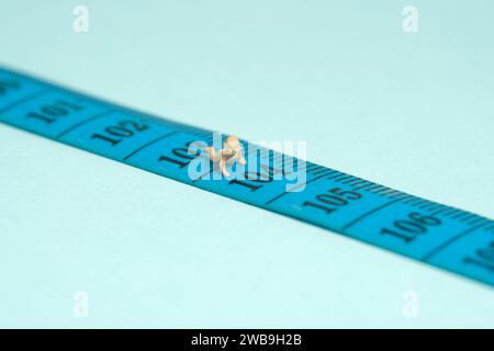 Miniature tiny people toy figure photography. Child growth period concept. A newborn infant baby crawling above measuring tape. Isolated on blue backg Stock Photo