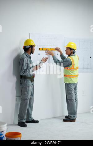 Builders in hardhats and uniform discussing blueprint hanging on wall Stock Photo