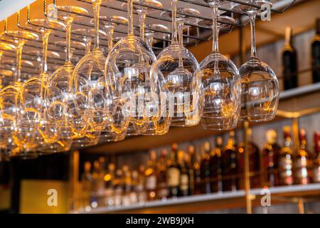 A group of wine glasses hanging upside down on a bar rack, bottles of liquor in the background Stock Photo