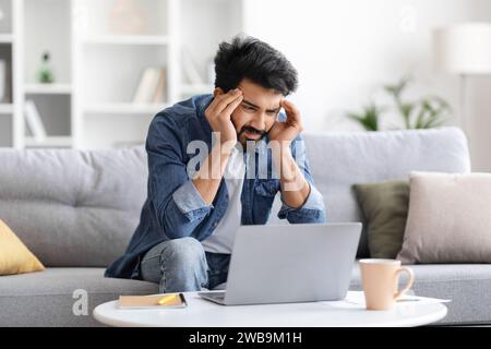 Stressed indian man having headache while working on laptop at home Stock Photo