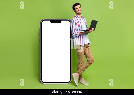 Full body photo of funny young it specialist programmer create new web application smartphone screen isolated on green color background Stock Photo