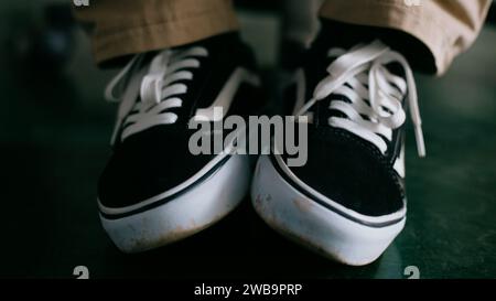 A pair of black and white sneakers with white laces, set against a brown pants background Stock Photo