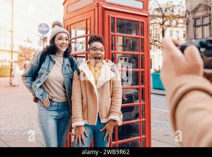 two friend, girlfriend, women using  camera and taking photos against a red phonebox in the city of England.Travel Lifestyle concept Stock Photo
