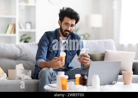 Young indian man holding bottle with pills and using smartphone Stock Photo