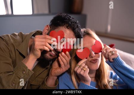 Valentine's Day. Close-up photo of happy couple in love hiding eyes behind paper hearts. Stock Photo