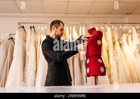 Male tailor or seamstress taking mannequin measurements for cloth pattern with measuring tape in fashion design studio, woman designer working with du Stock Photo