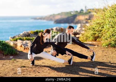 Man and woman doing side lunges by the sea at sunny day Stock Photo
