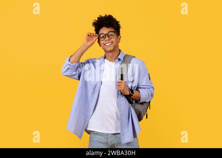 Confident black student adjusting glasses on a yellow background Stock Photo