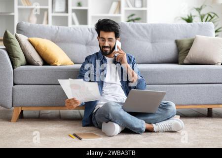 Focused indian man working from home, talking on phone and analyzing documents Stock Photo