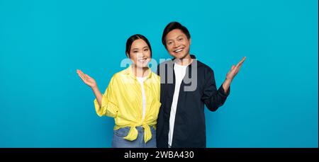 Smiling Asian man and woman standing with palms open in a welcoming gesture Stock Photo