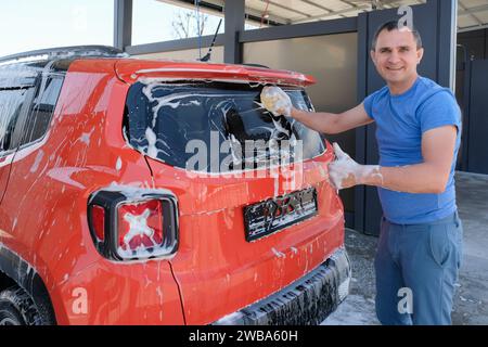 Happy man washes a car at a car wash. Car in foam Stock Photo