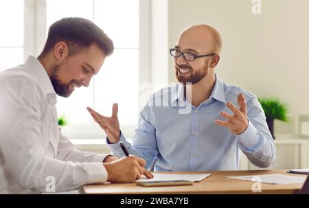 Two smiling businessmen sitting together at desk in office working on documents Stock Photo