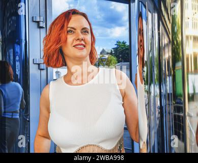 Friendly attractive young redhead woman relaxing leaning against wall with copy space in an urban street staring at camera Stock Photo